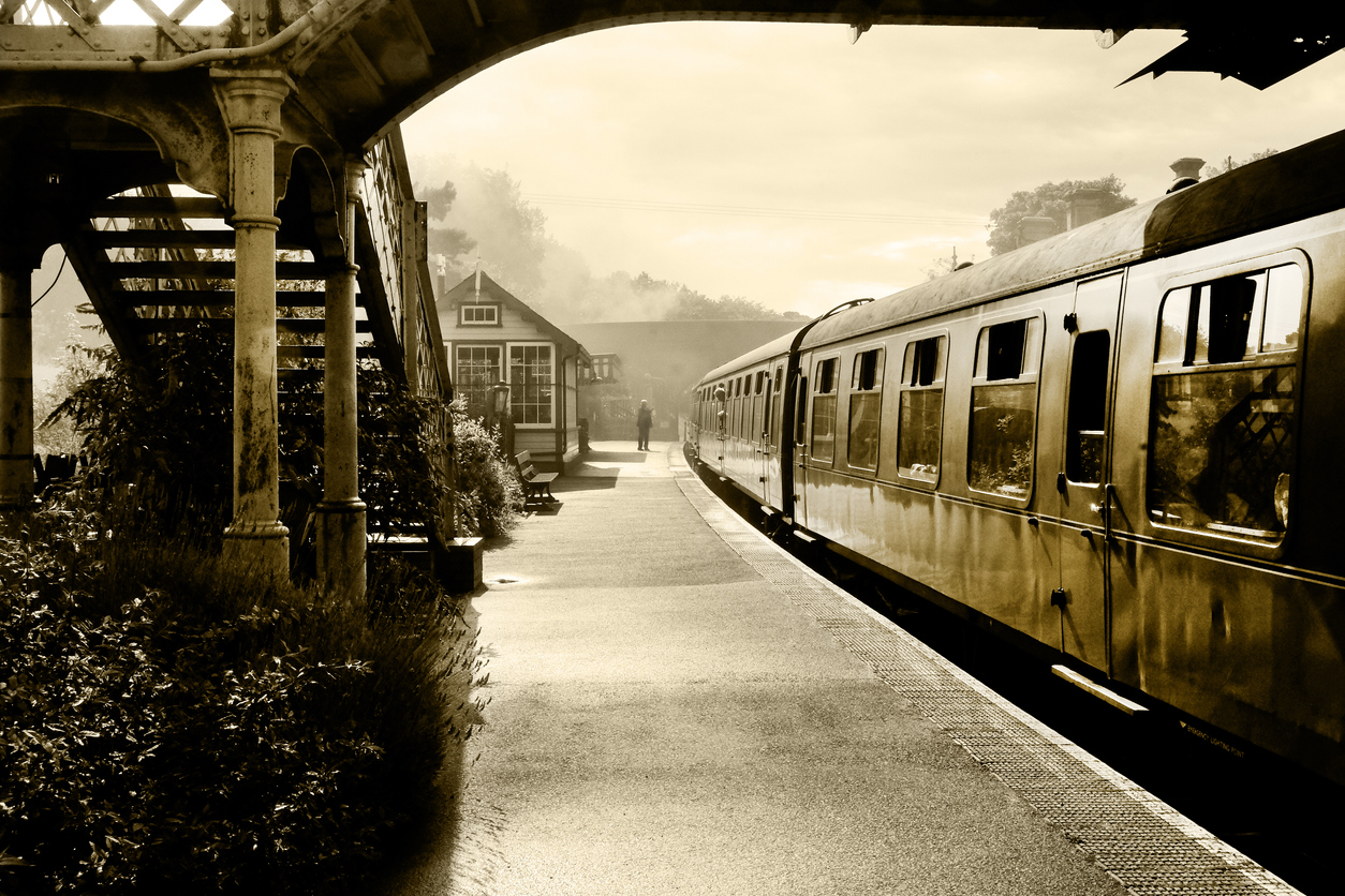black and white retrospective photograph of a steam train and carraiges at Weybourne station, Norfolk, England, UK, the platform is misty and in the distance is the gaurd and signal box